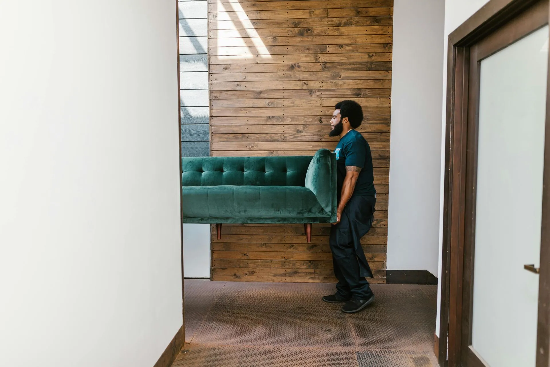 Mover carrying a green velvet sofa down a hallway