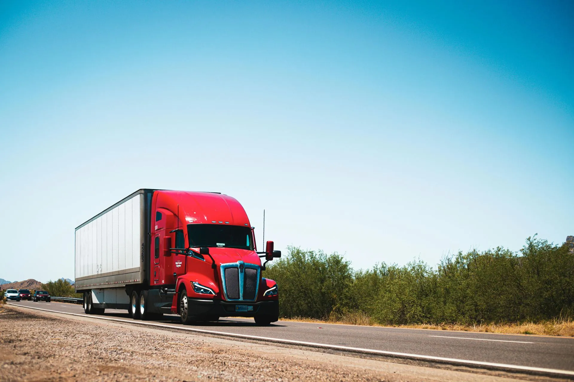Red semi-truck pulling a white trailer down an open highway