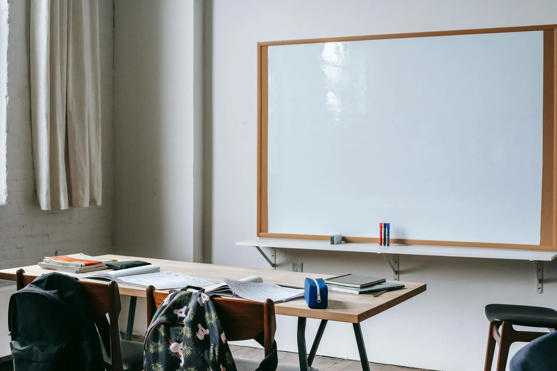Classroom with a whiteboard, a desk of books and backpacks on the chairs